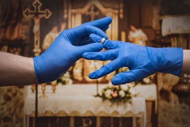 The young couple puts on wedding rings wearing protective gloves. Marriage during a coronavirus epid...