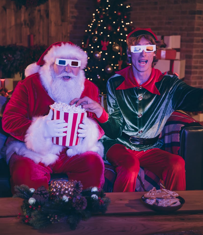 Photo portrait of santa claus and elf eating popcorn using remote watching movie on sofa in 3d glass...
