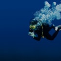 Recreational scuba diver with yellow mask, cloud of bubbles in black neoprene suit taking underwater...