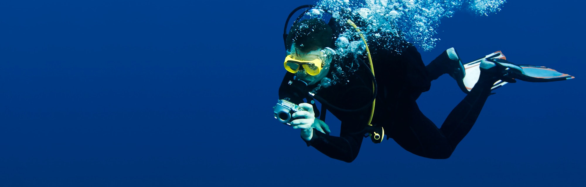 Recreational scuba diver with yellow mask, cloud of bubbles in black neoprene suit taking underwater...