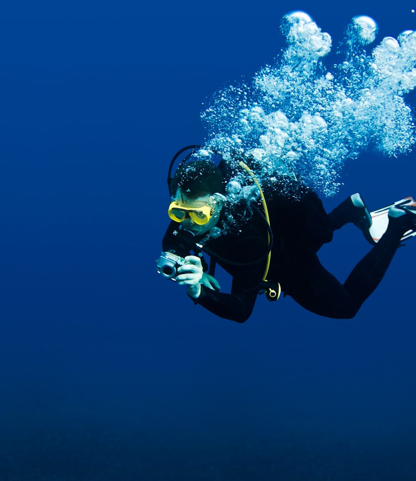 Recreational scuba diver with yellow mask, cloud of bubbles in black neoprene suit taking underwater...