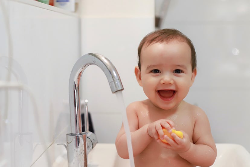 Baby smiles to camera while playing in the sink, in a story about Capricorn names.