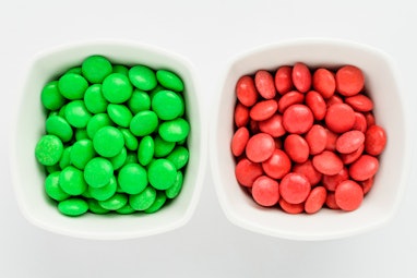 Two squared bowls with small green and red coated chocolate candies similar to m&ms in a squared bow...