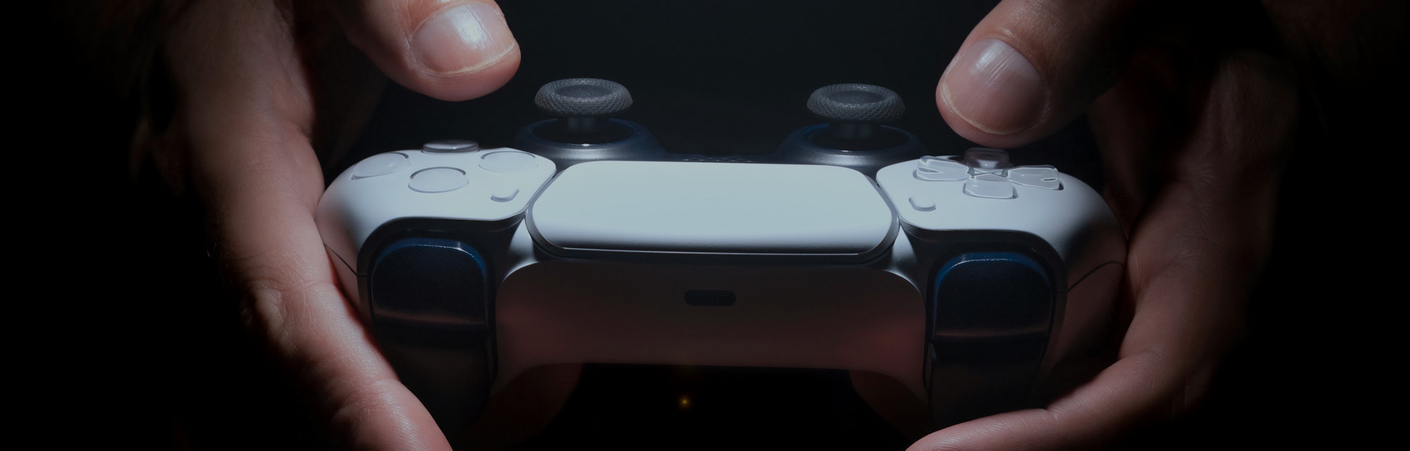 Hands holding a PS5 game controller with spot light.