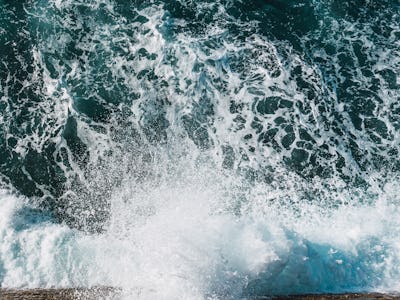 ocean waves breaking on the rocks. the water is dark with a lot of white foam that forms when breaki...