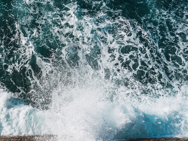 ocean waves breaking on the rocks. the water is dark with a lot of white foam that forms when breaki...