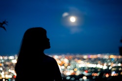 The silhouette of a woman looking at the full moon rising over the city. December's full moon takes ...