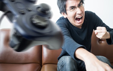 An Asian young man throwing video game controller away with anger; Concept of aggressive serious gam...