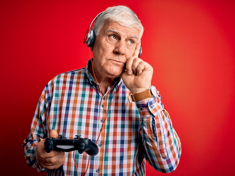 Senior handsome hoary gamer man playing video game using joystick and headphones serious face thinki...