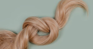 Blonde hair lock tied in knot. Strand of honey blonde hair on mint background, top view. Hairdresser...