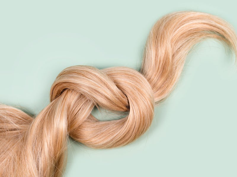 Blonde hair lock tied in knot. Strand of honey blonde hair on mint background, top view. Hairdresser...