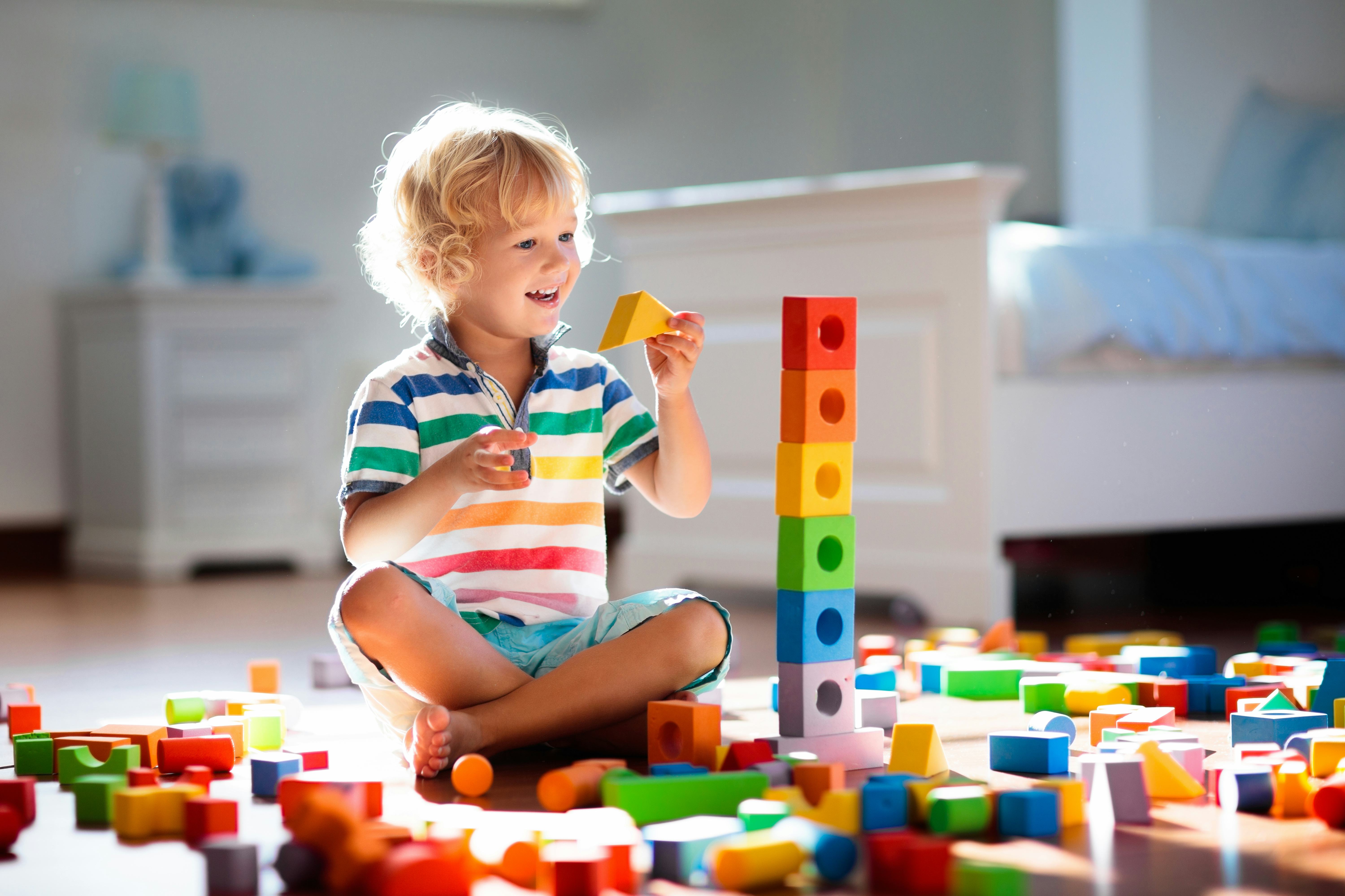 Child playing with colorful toy blocks. Kids play. Little boy building tower of block toys sitting o...
