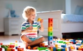 Child playing with colorful toy blocks. Kids play. Little boy building tower of block toys sitting o...