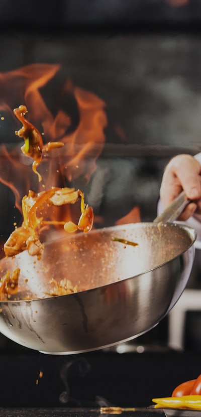 Chef hands keep wok with fire. Closeup chef hands cook food with fire. Chef man burn food at profess...