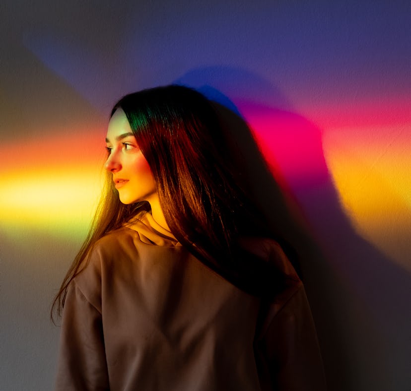 Young woman basking in rainbow light after reading her January 3, 2022 weekly horoscope for her zodi...