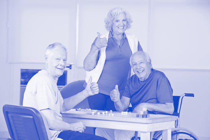 Three happy senior people in nursing home holding thumbs up and playing Bingo