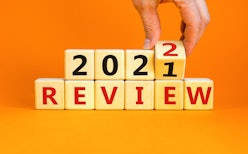 2022 review new year symbol. Businessman turns a wooden cube and changes words 'Review 2021' to 'Rev...