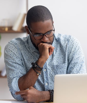 Head shot serious puzzled African American businessman looking at laptop screen sitting in office. E...