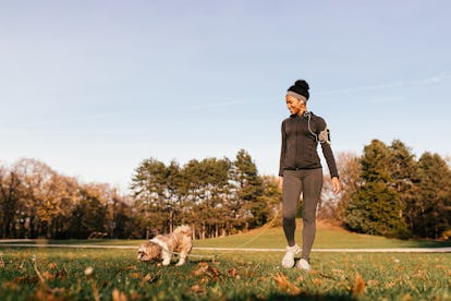 Happy African American athletic woman enjoying while walking her dog in nature.