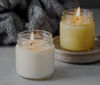 Burning candles on grey table, space for text. Grey knitted scarf and scented candles. Cozy winter a...