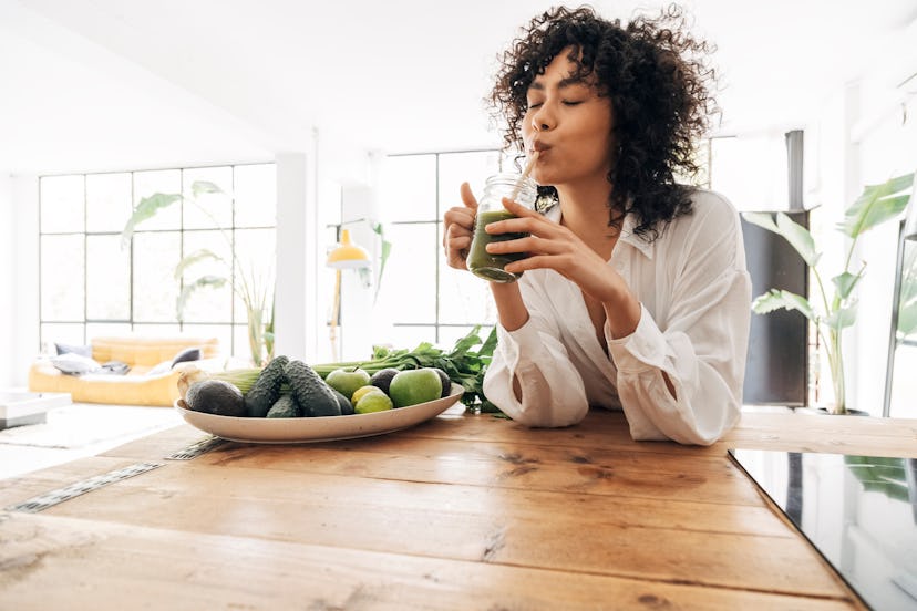 Young woman drinking green juice with reusable bamboo straw.