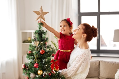 A woman holding a child as she decorates a Christmas tree, demonstrating how to keep artificial Chri...