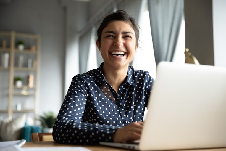 Cheerful indian girl student professional laughing looking away sit with laptop computer at home off...