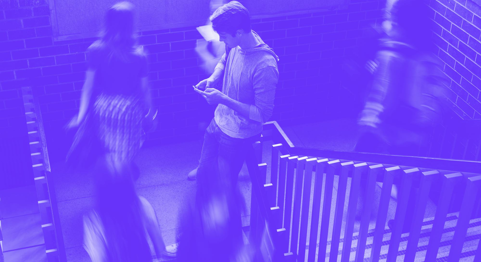 Young man standing on the staircase in college with girls walking by. Students on steps of college c...