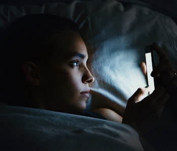 Young beautiful woman in bed using mobile phone late at night at dark bedroom, internet addiction co...