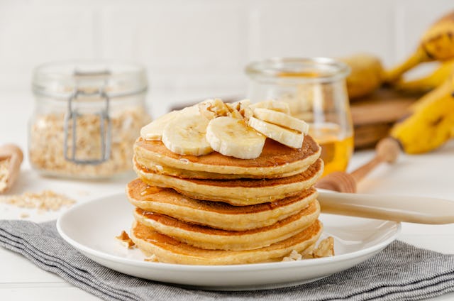 A stack of oatmeal banana pancakes with slices of fresh bananas, walnuts and honey on top with cup o...