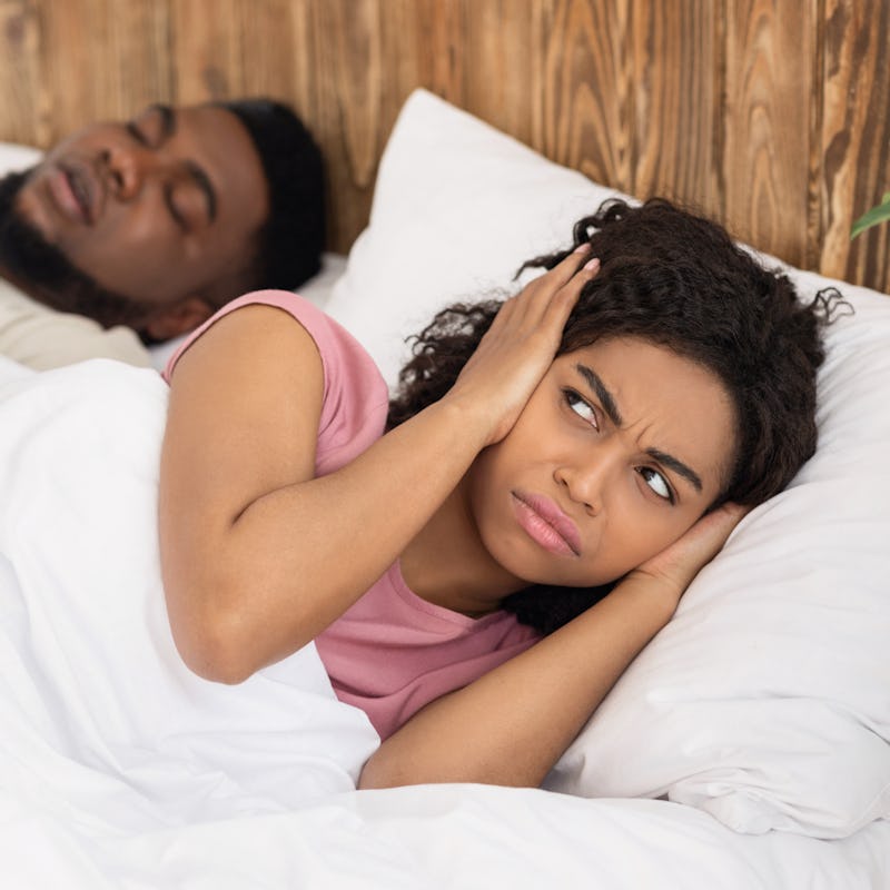 Annoyed misophoniac woman covering her ears with palms while her partner is snoring.