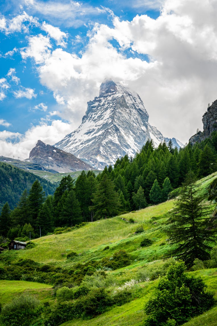 Vertical scenic view of the Matterhorn mountain summit with snow clouds blue sky and green nature du...