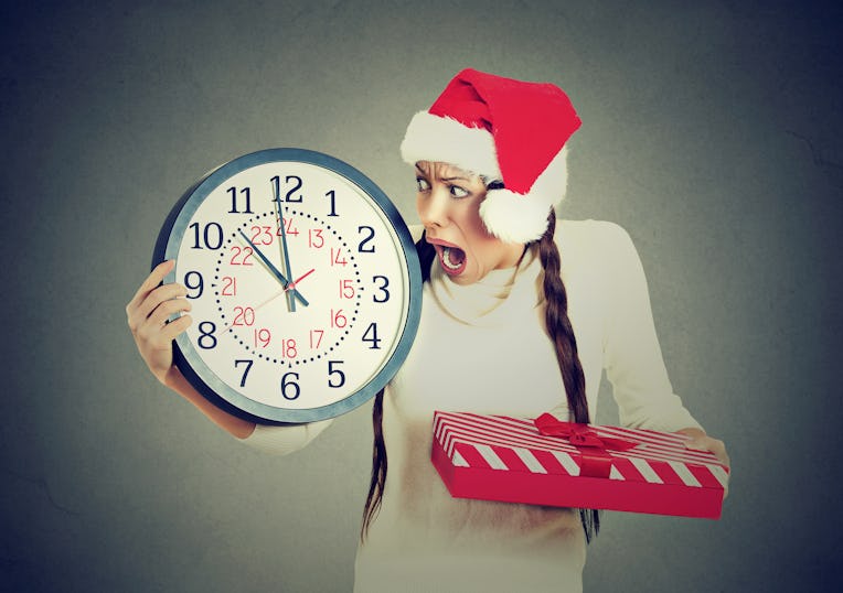 Closeup portrait worried stressed in a hurry young woman wearing red santa claus hat holding clock g...