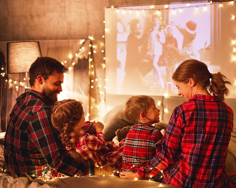 happy family in checkered pajamas: mother father and children watching projector, film, movies with ...