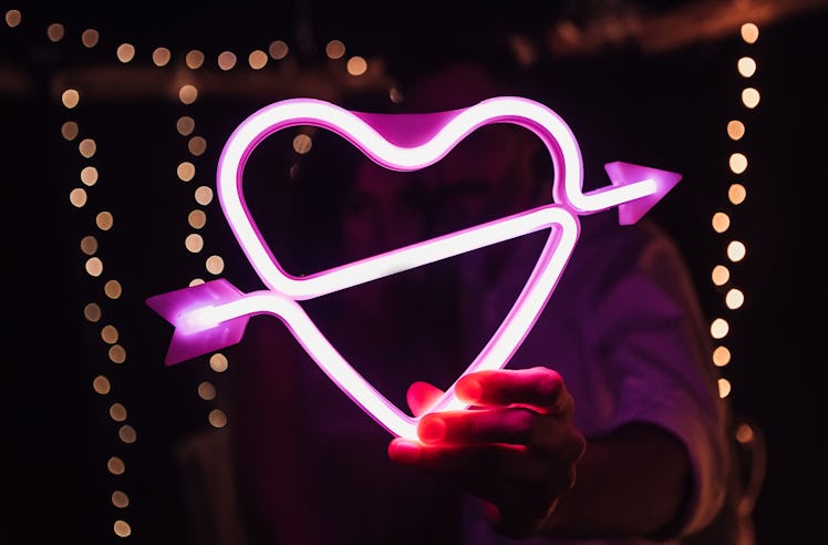 Glowing bright luminous neon heart sign pierced by cupid arrow, amour shape in vivid colors. Newlywe...