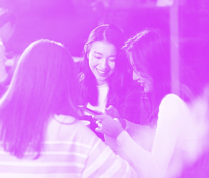 three happy beautiful young asian women sitting at table chatting talking playing with cellphone in ...