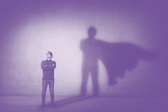 Brave man keeps arms crossed, looks confident, casting a superhero with cape shadow on the wall. Amb...