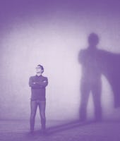 Brave man keeps arms crossed, looks confident, casting a superhero with cape shadow on the wall. Amb...