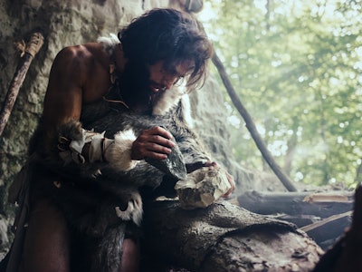 Primeval Caveman Wearing Animal Skin Hits Rock with Sharp Stone and Makes First Primitive Tool for H...