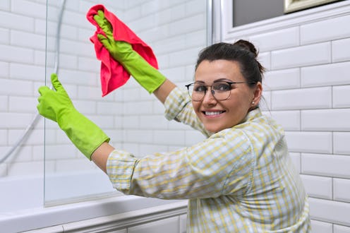 Woman doing cleaning in the bathroom, at home. Female cleaning polishing shower glass with a washclo...