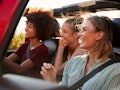 Three female friends on a road trip drive together in an open jeep while on a road trip.