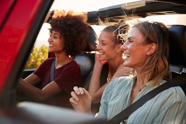 Three female friends on a road trip drive together in an open jeep while on a road trip.