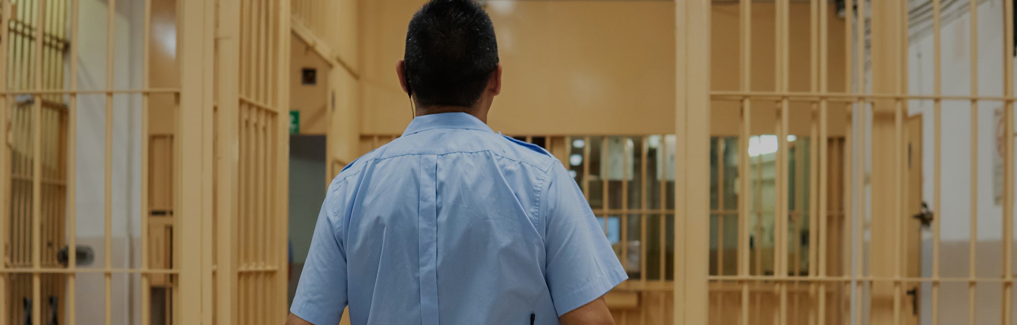 Jailer walking through the prison aisle, entering the safe zone. Prison officer in blue shirt with ...