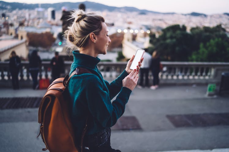 A happy woman looks at her phone while vacationing in a different city. 