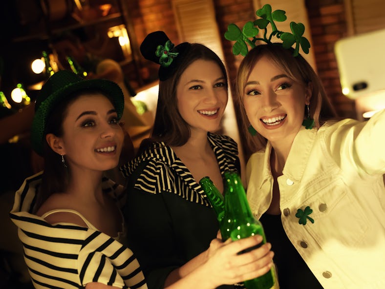 A group of friends pose for a selfie with some beer in a bar on St. Patrick's Day for a St. Patrick’...