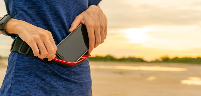 Young Asian woman keep smartphone in waist bag before running cardio exercise in the morning. Outdoo...