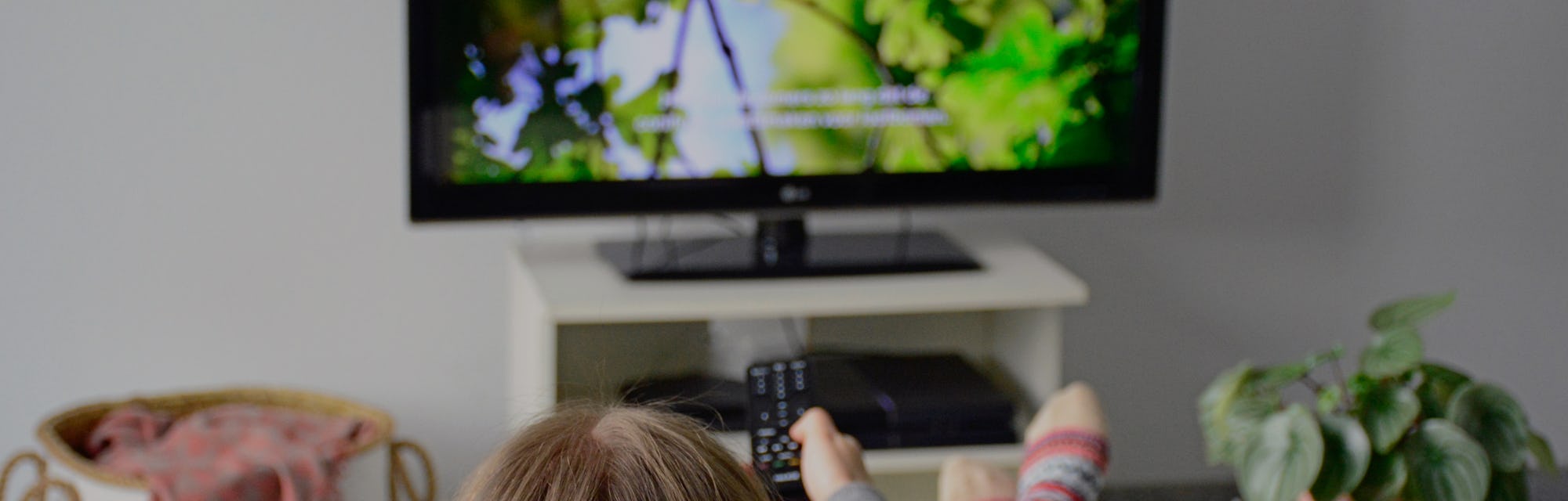Young woman watching television with subtitles while sitting comfortably on sofa at home in living r...