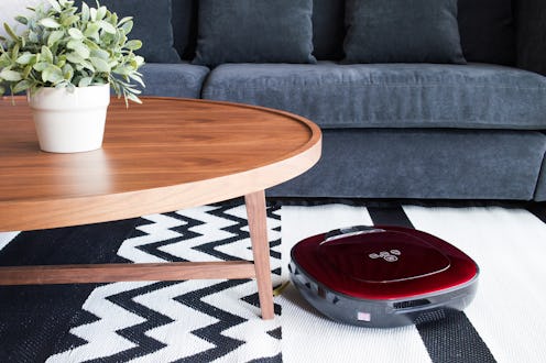 Robotic vacuum cleaner on carpet in cozy living room with navy blue sofa and wooden table