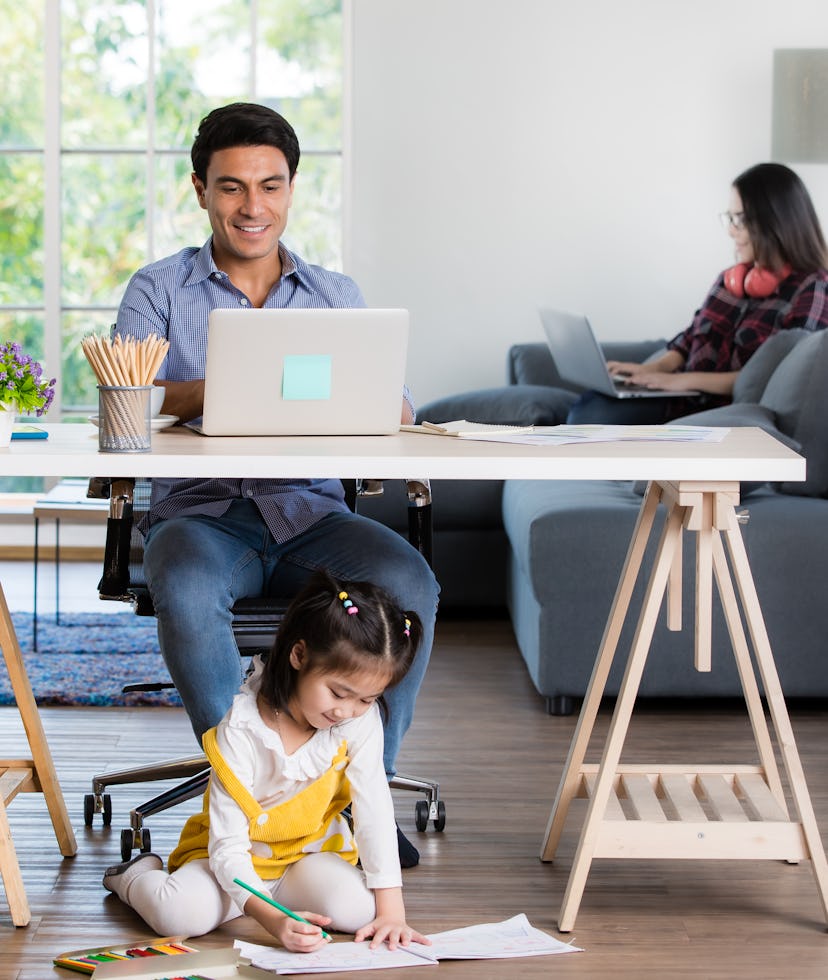 Mixed race family sharing time in living room. Caucasian father using notebook computer to work and ...