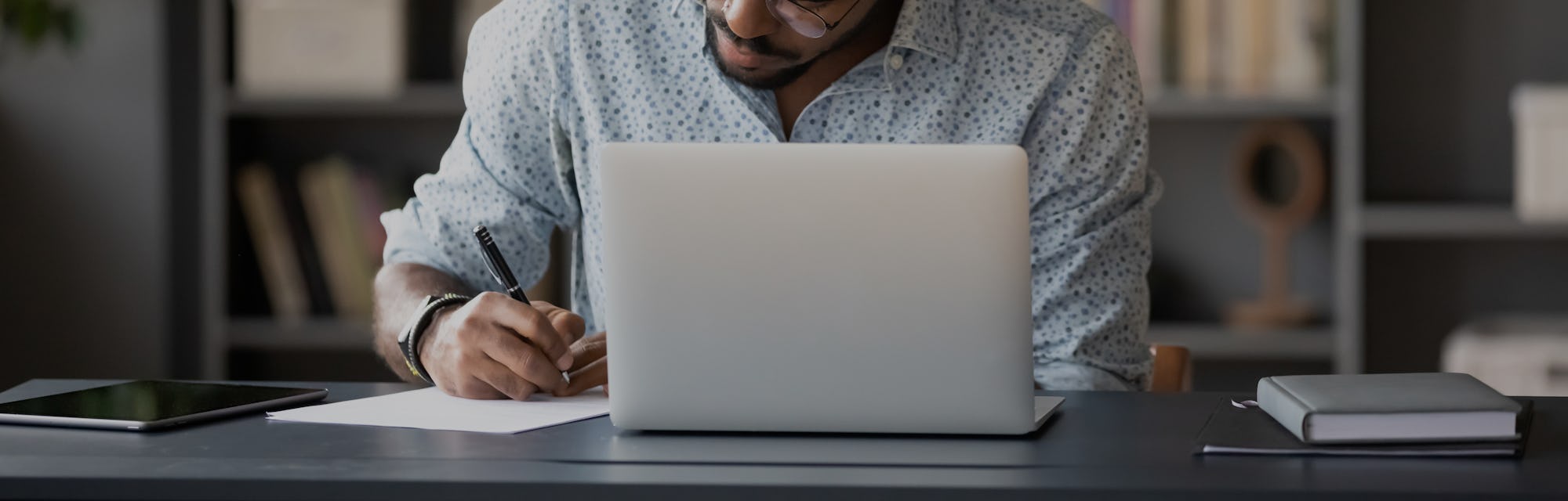 Concentrated African American male worker sit at desk handwrite watching webinar or training on lapt...